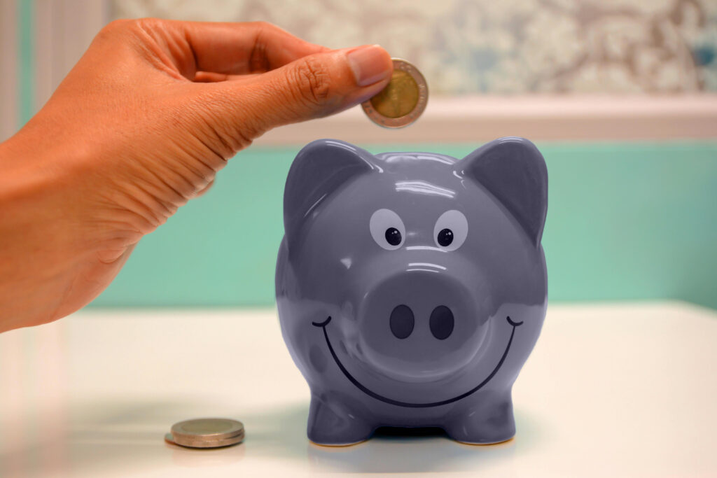 person inserting money into purple piggybank