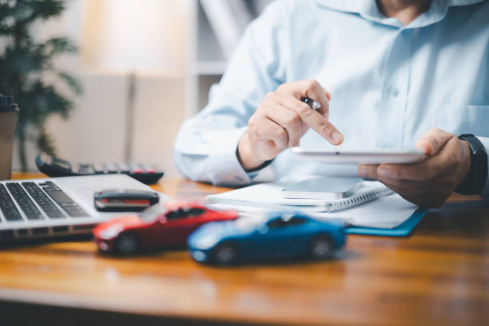 a man doing calculations at a desk with toy cars sitting on it
